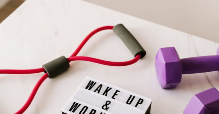 Tape Sculpting - From above composition of dumbbells and massage double ball and tape and tubular expanders surrounding light box with wake up and workout words placed on white surface of table