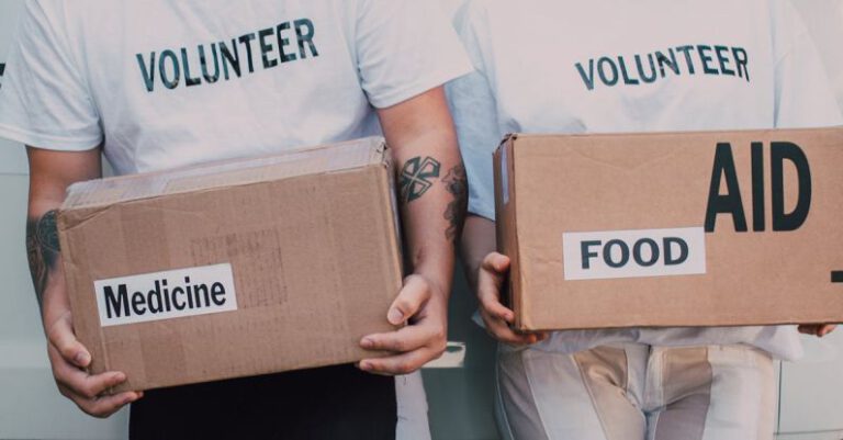 Social Impact - Man and Woman Carrying Medicine and Food Labelled Cardboard Boxes Behind a White Van