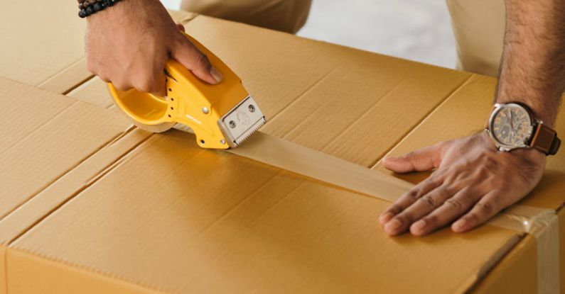 Custom Tape - Unrecognizable man sealing box with duck tape while preparing for moving out